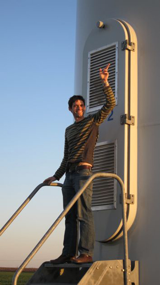 a man stands in front of a windmill's base and waves, as if he were the president getting out of Air Force One
