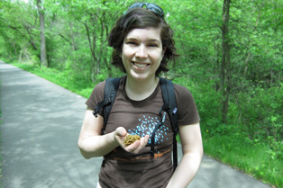 Martha, wearing in a brown t-shirt, holds a morel mushroom in hand