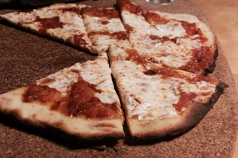 thin crust cheese pizza on a cork serving board